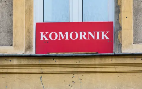 Czerwona tablica z napisem "KOMORNIK" na tle okna. Może to oznaczać zajęcie komornicze wynagrodzenia.