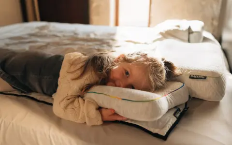 Ein kleines Mädchen kuschelt sich auf einem Bett an ein Kissen. Die Schlafphasen von Kindern sind wichtig für ihre Entwicklung.