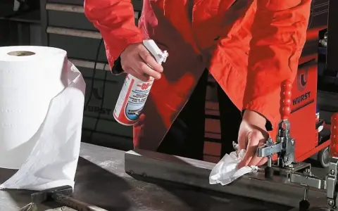 Osoba w pomarańczowej kurtce pokazuje, jak czyścić biżuterię ze stali chirurgicznej, używając sprayu i papierowego ręcznika.