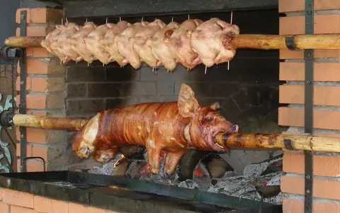 Ein Spanferkel grillen über offenem Feuer. Darüber hängen mehrere Hähnchen am Spieß.