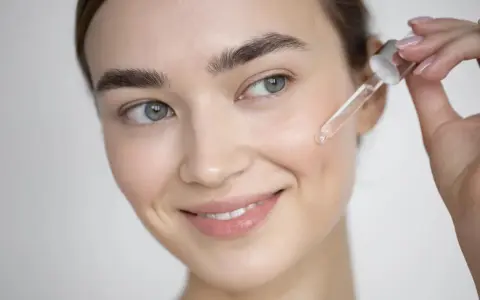 Una mujer sonríe mientras aplica un suero con antioxidantes faciales en su piel con un gotero.