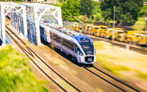 Nowoczesny pociąg PKP Intercity z niebieskim przodem mija biały most kolejowy.