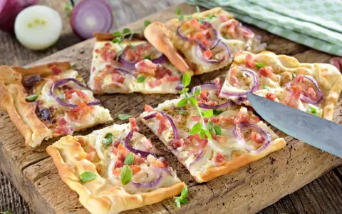 Kawałki pizzy z cebulą i boczkiem na drewnianej desce.