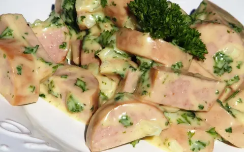 Une délicieuse salade de cervelas, coupée en dés et nappée d'une sauce crémeuse aux herbes fraîches, garnie d'un brin de persil.