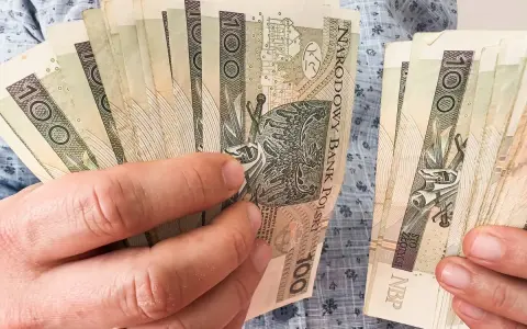 Ręce trzymające plik banknotów 100 zł. Planowanie finansowe, jak wybrać najkorzystniejsze lata do emerytury, wymaga analizy oszczędności.
