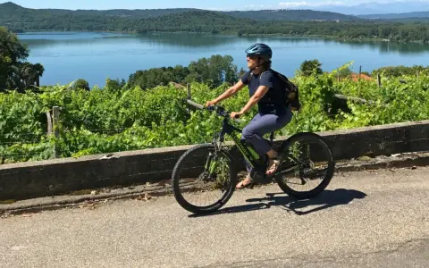 Donna in bici elettrica lungo il cammino di Oropa, tra vigneti e un lago sullo sfondo.