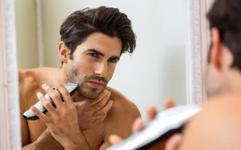 Hombre se afeita a contrapelo con una recortadora, mirándose en el espejo.