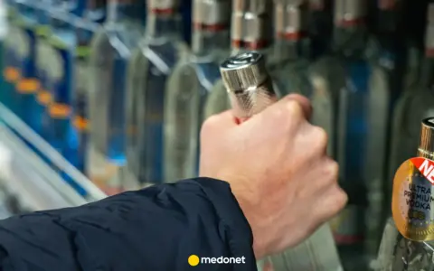 Dłoń sięga po butelkę wódki, a artykuł na medonet.pl analizuje wpływ alkoholu, w tym piwa, na białe krwinki.