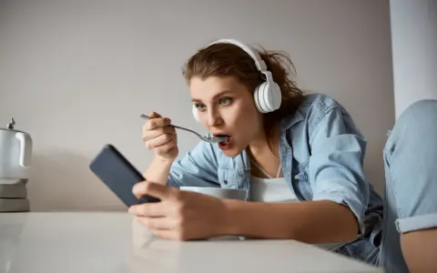 Młoda kobieta w słuchawkach je płatki, patrząc w telefon. Czy to objawy fonoholizmu?