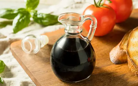 Mały dzbanuszek z ciemnym, gęstym **octem balsamicznym** obok pomidorów, bazylii i grzanek.