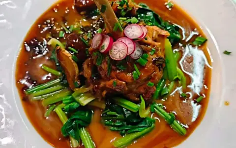 Un plat savoureux, un os de viande braisé dans une sauce riche, garni de radis et de légumes verts. Un aperçu des spécialités parisiennes.
