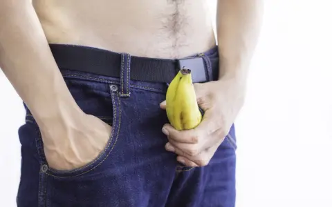 Mężczyzna w dżinsach trzyma banana, sugerując jelqing efekty.