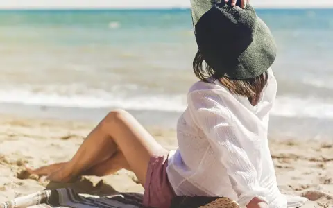 Kobieta w kapeluszu siedzi na plaży, ciesząc się spokojnymi miejscami nad morzem. Słońce i szum fal tworzą idealną atmosferę relaksu.