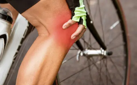 Cyclist holding knee with red pain indicator. Learn about cycling knee pain exercises to get back on the road.