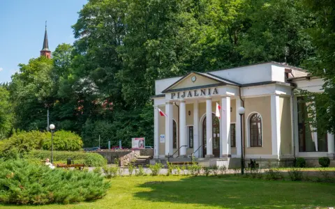 Duszniki Zdrój atrakcje: Pijalnia wód mineralnych z kolumnadą i wieżą kościelną w tle.