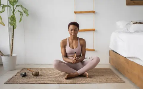 Mujer meditando en postura de loto, con los ojos cerrados y un palo de incienso en las manos. A su lado, un cuenco tibetano y una vela. Aprende como meditar para encontrar la paz interior.