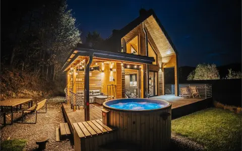 Drewniany domek z jacuzzi i tarasem, idealne miejsce na babia góra noclegi. Oświetlony girlandami, zaprasza do relaksu.