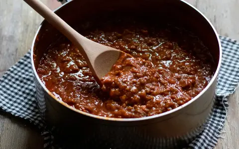 Un pentolino pieno di profumato ragù di carne, pronto per condire la pasta. Un cucchiaio di legno mescola la salsa densa e invitante.