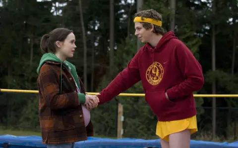 Una ragazza incinta e un ragazzo con fascia gialla si tengono per mano, scena tipica dei film d'amore adolescenziali.