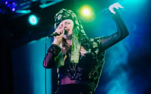 Amanda Jenssen konsert. Hon sjunger med en mikrofon i handen, klädd i en blommig scarf och en glittrig topp.
