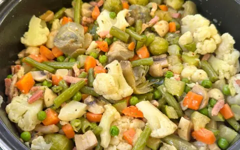 Un plato abundante de menestra de verduras, con brócoli, zanahoria, judías verdes, guisantes y trozos de tocino.