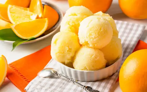 Erfrischendes orangen sorbet in einer Schale, umgeben von frischen Orangen und saftigen Orangenstücken. Ein Löffel liegt bereit.