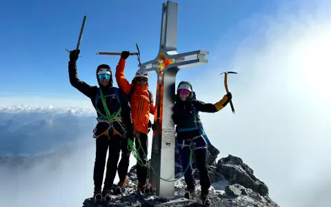 Drei Bergsteiger feiern am Gipfelkreuz des Ortler Normalwegs ihren Erfolg.