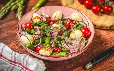 Frischer Spargelsalat mit Ei, Tomaten, roten Zwiebeln und Mozzarella-Kugeln, beträufelt mit Balsamico-Dressing.