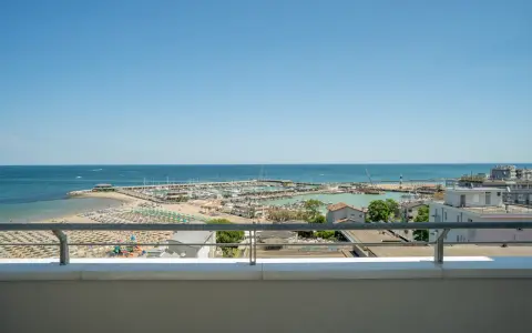 Vista dal balcone dell'hotel Acropolis Cattolica: spiaggia, porto turistico e mare azzurro sotto un cielo limpido.