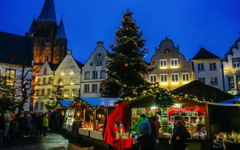 Festlicher Weihnachtsmarkt mit beleuchtetem Baum und Buden vor historischen Häusern. Ein Kandidat für den besten Weihnachtsmarkt NRW.