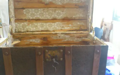 Proceso de restaurar baúl antiguo de chapa y madera. El interior muestra madera desgastada y papel tapiz despegado.