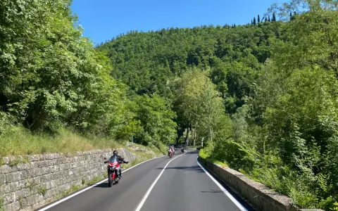 Motociclisti su strade panoramiche in Emilia Romagna, tra colline verdi e cielo azzurro.