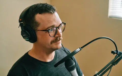 Mężczyzna w okularach i słuchawkach Sony nagrywa podcast. Dba o odpowiedni gain staging, by dźwięk był czysty.
