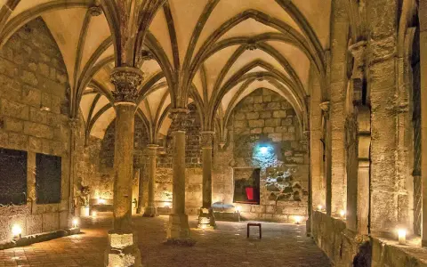 Gewölbte Gänge in einem **kloster mittelalter**. Säulen tragen das steinerne Dach, Kerzenlicht erhellt den Boden.