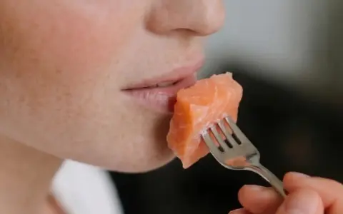 Une personne mange un morceau de saumon à la fourchette. Un aperçu de son visage, idéal pour un avis sur le régime Natman.