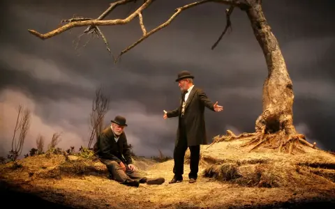 Due uomini, forse Vladimir ed Estragon, attendono Godot sotto un albero spoglio.