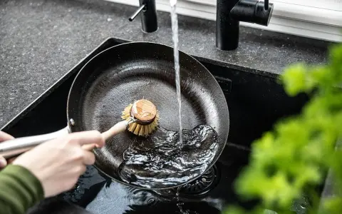 Mycie patelni żeliwnej pod bieżącą wodą za pomocą szczotki.