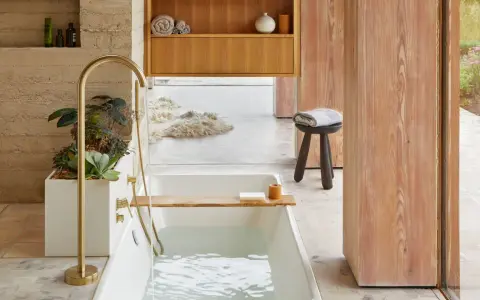 Bain relaxant avec baignoire remplie, robinetterie dorée, plantes et bois. Une belle inspiration salle de bain.