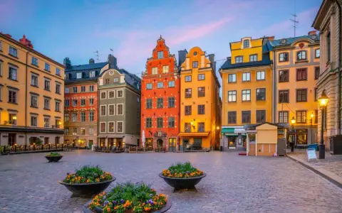 Färgglada hus på ett kullerstens torg i Gamla Stan, Stockholm, med blomkrukor i förgrunden.
