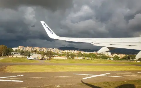 Skrzydło samolotu Ryanair nad lotniskiem, ciemne chmury na niebie.