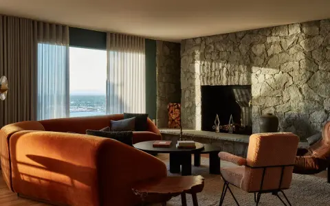 Sofá curvo naranja y chimenea de piedra, con un toque de diseño años 50.