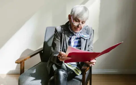 Une femme âgée, en pleine retraite, examine des documents artistiques dans un dossier rouge.