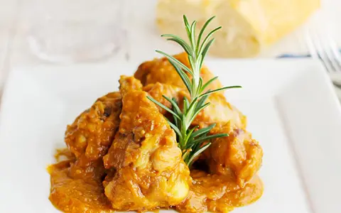Sabroso pollo con almendras en una salsa dorada, adornado con romero fresco. Un plato que invita a disfrutar.