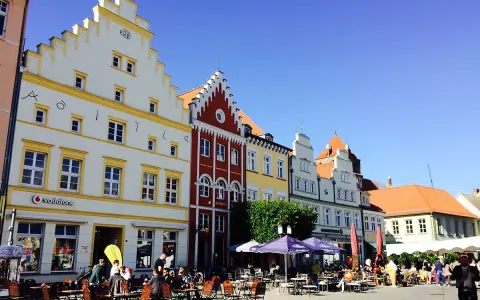 Bunte Häuserfronten säumen den mv markt. Menschen sitzen in Cafés unter Sonnenschirmen und genießen den sonnigen Tag.
