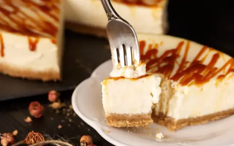Une fourchette prélève un morceau crémeux de cheesecake, révélant le fromage frais onctueux sous un filet de caramel.