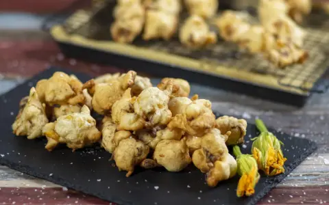 Frittelle di fiori di zucca dorate e croccanti, servite su una lavagna con fiori freschi e sale grosso.
