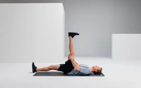 Mann liegt auf Matte, dehnt Bein für Hamstring Training.