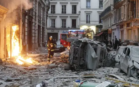 Un pompier avance dans les décombres d'une explosion gaz Paris. Des voitures détruites et des flammes ravagent la rue.