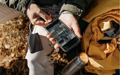 Un homme charge son téléphone avec une batterie externe, une aide précieuse pour comment organiser son téléphone et ses photos en voyage.