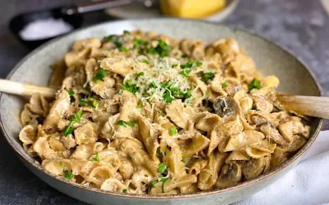 En krämig kyckling svamp pasta i en skål, toppad med persilja och parmesan.